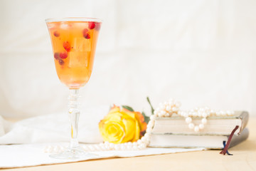 Glass of cranberry cocktail with vintage books and pearls