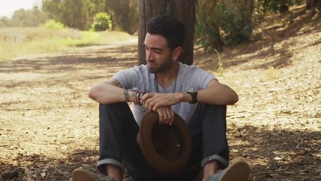 Rugged hispanic man sitting outdoors holding hat