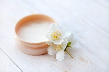 Fototapeta na wymiar Pot of beauty cream with jasmine blossom on white wooden table close up