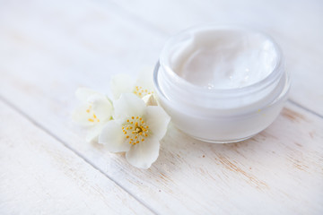 Fototapeta na wymiar face cream with jasmine blossom on white wooden table