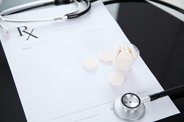 Stethoscope and prescription and pills, black reflective background