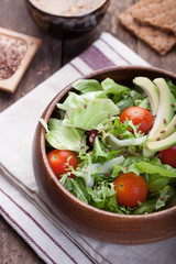 Salad with lettuce, tomatoes, flax seeds and avocado in a wooden bowl.