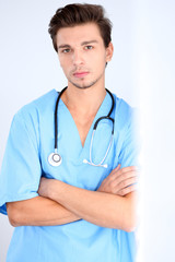 Attractive male doctor standing near the wall, crossed arms