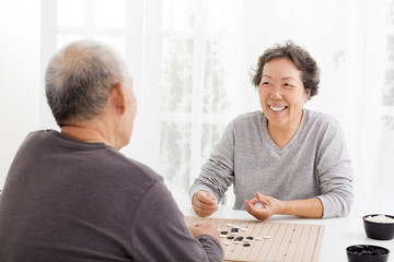 happy asian senior couple playing chess in living room
