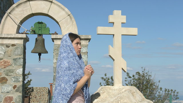Peaceful young woman praying outdoors near stone cross, asking God for blessing