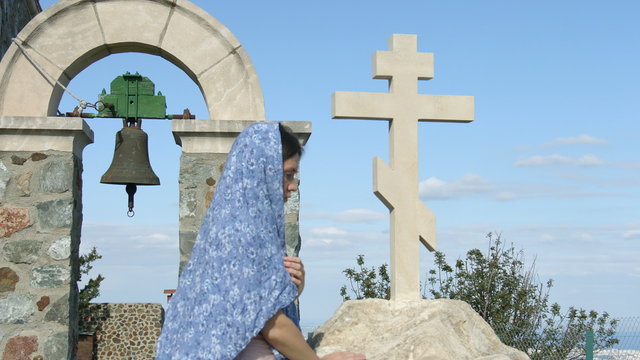 Young female parishioner saying prayers outside church, touching stone cross