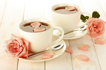 Two cups of tea with creamy roses on white wooden table