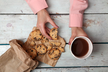 Female hands holding cup of coffee and cookies on wooden table close up