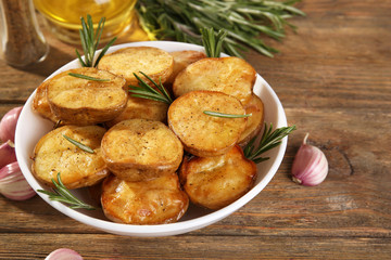 Delicious baked potato with rosemary in bowl on table close up
