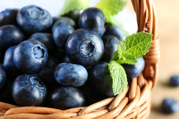 Tasty ripe blueberries with green leaves in basket close up