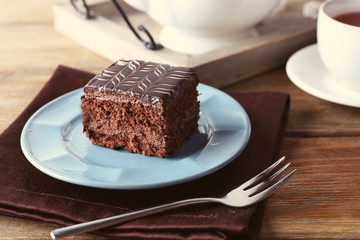 Sweet chocolate cake on blue plate with cup of tea on brown cotton serviette, close up