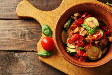Tasty vegetarian ratatouille made of eggplants, squash, tomatoes in bowl on wooden table background