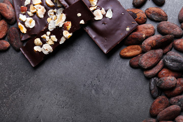 Black chocolate pieces with nuts and cocoa beans on dark gray background