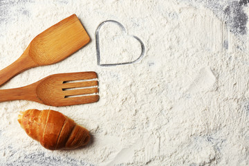Heart of flour, croissant and  wooden kitchen utensils n on gray background