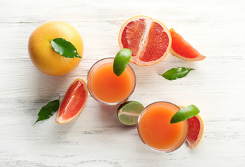 Two glasses of citrus juice and fresh fruits on light wooden background