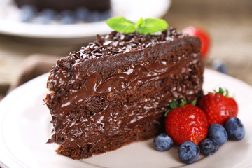 Chocolate cake with chocolate cream and fresh berries on plate, on wooden background
