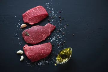 Photo sur Plexiglas Viande Steaks de viande marbrés crus avec assaisonnements, surface en bois noire