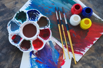 brushes and color palette with painting on rustic wooden background, close up