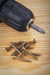 cordless drill and large screws on a wood background