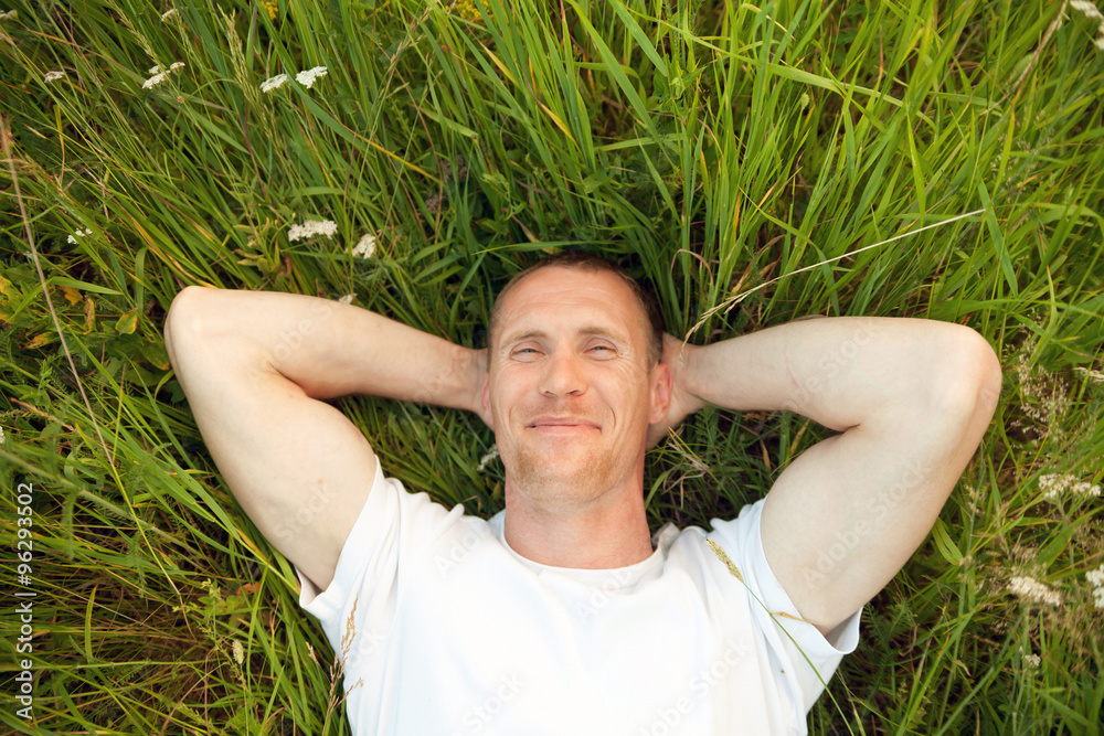 Wall mural Smiling man lying in summer grass