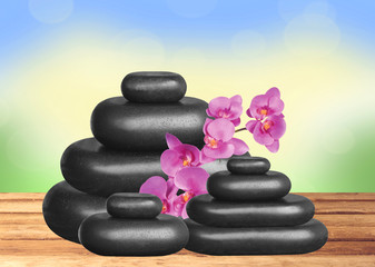 Black spa stones and pink orchid on wooden table over nature bac