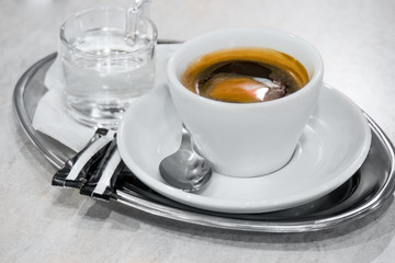 Americano coffee and small glass  of water on metal shallow tray