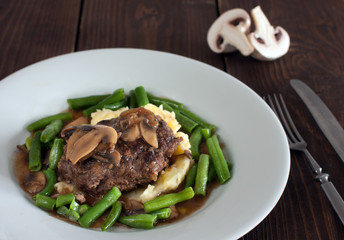 A plate of salisbury steak with mashed potatoes, green beans and mushrooms