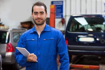 Young attractive mechanic working at the garage - obrazy, fototapety, plakaty