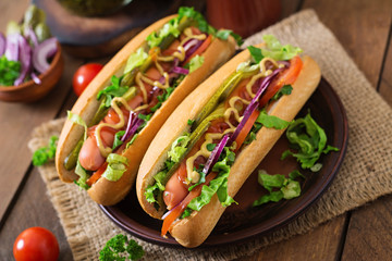 Hot dog with pickles, tomato and lettuce on wooden background