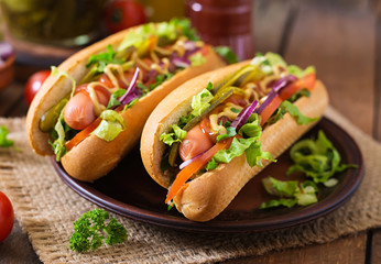 Hot dog with pickles, tomato and lettuce on wooden background