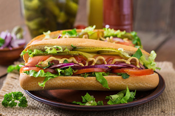 Hot dog with pickles, tomato and lettuce on wooden background