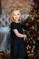 Little girl in black dress near Christmas tree