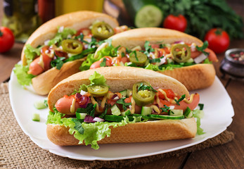 Hot dog with jalapeno peppers, tomato, cucumber and lettuce on wooden background