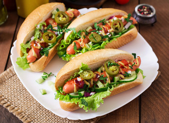 Hot dog with jalapeno peppers, tomato, cucumber and lettuce on wooden background