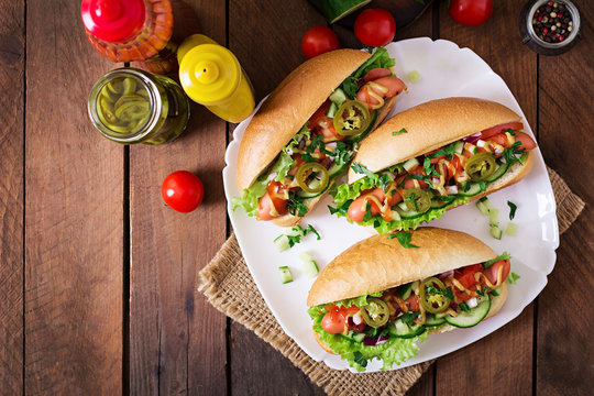 Hot dog with jalapeno peppers, tomato, cucumber and lettuce on wooden background