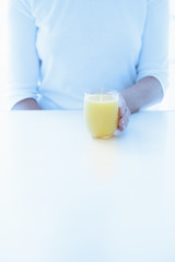 Cropped view of a woman holding a chilled glass of fresh orange juice on a white counter.