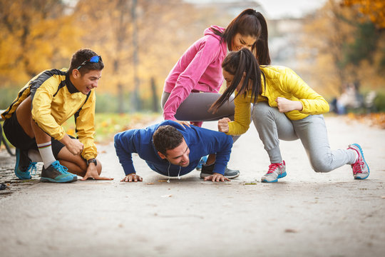 The group of friends is now having a blast in the park, attempting to do push-ups amidst laughter and shared enjoyment of the autumn day.