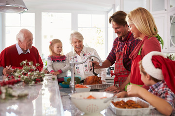 Extended Family Group Basting Christmas Turkey In Kitchen