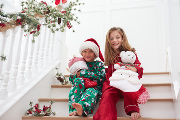 Two Children Sitting On Stairs In Pajamas At Christmas