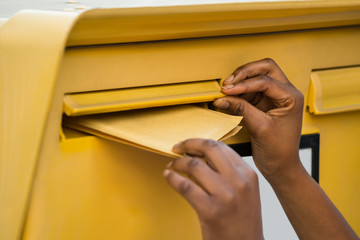 Person's Hand Inserting Letter In Mailbox