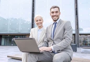 smiling businesspeople with laptop outdoors