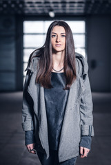 Obraz na płótnie Canvas young woman with long hair, with a leather backpack, a warm hat, beautiful makeup, leather pants, a gray sweatshirt and a leather shirt, high heels walking one in the production hall and the street