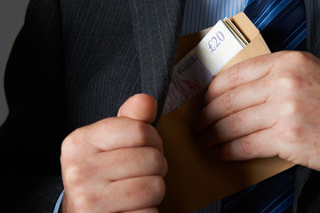 Businessman Putting Envelope Of Sterline Notes In Jacket Pocket