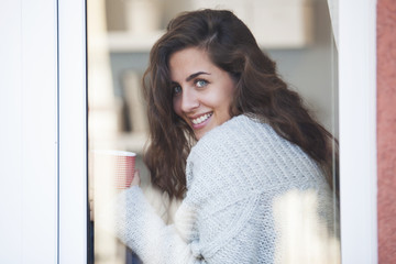 Young beautifuk woman drinking coffee and looking out of the window
