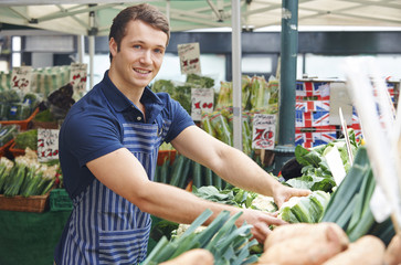 Man Arranging Display On Market Vegetable Stall