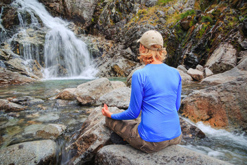 girl in lotus pose looking at waterfall. Travel concept