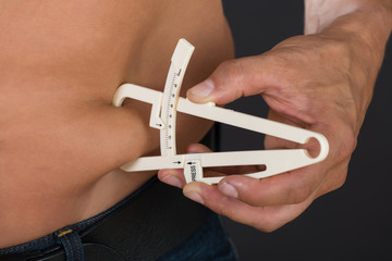 Shirtless Man Measuring Stomach Fat With Caliper
