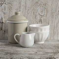 Vintage crockery - enamel jug and white ceramic bowl on bright wooden surface. Rustic style