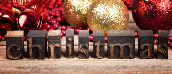 The word CHRISTMAS written with vintage wood printer blocks. Christmas message over old wood with traditional tree decorations behind.