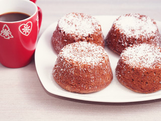 Chocolate muffins with iced sugar on a wooden table with red coffee cup with winter design